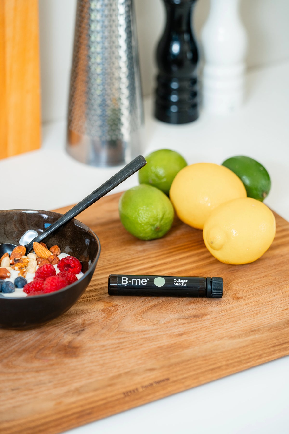 Yogurt breakfast with blueberries, raspberries, and nuts alongside B.me Collagen Matcha shot, lemons, and a kitchen setting