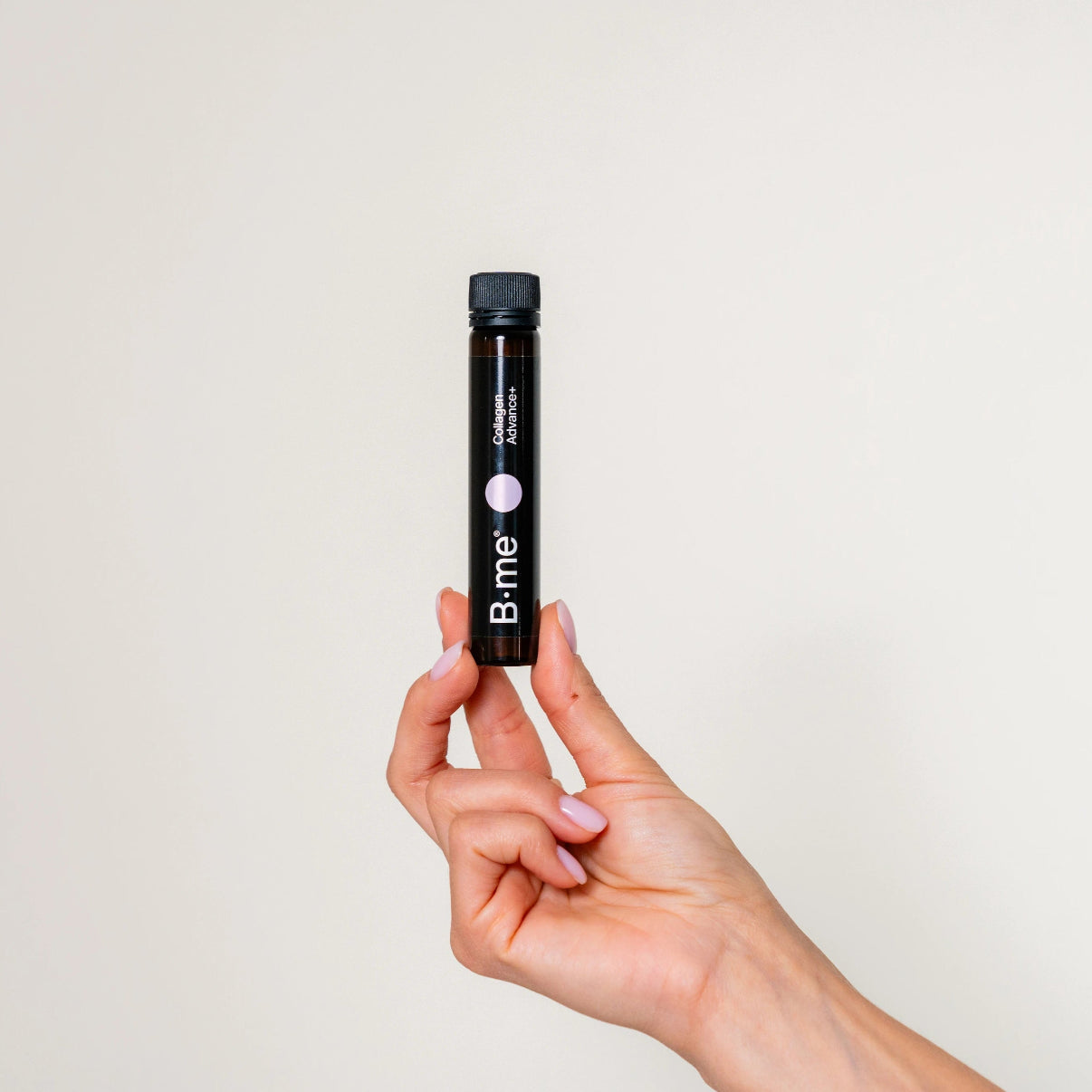 One hand with pink gel nails holding B.me Collagen Advance+ shot