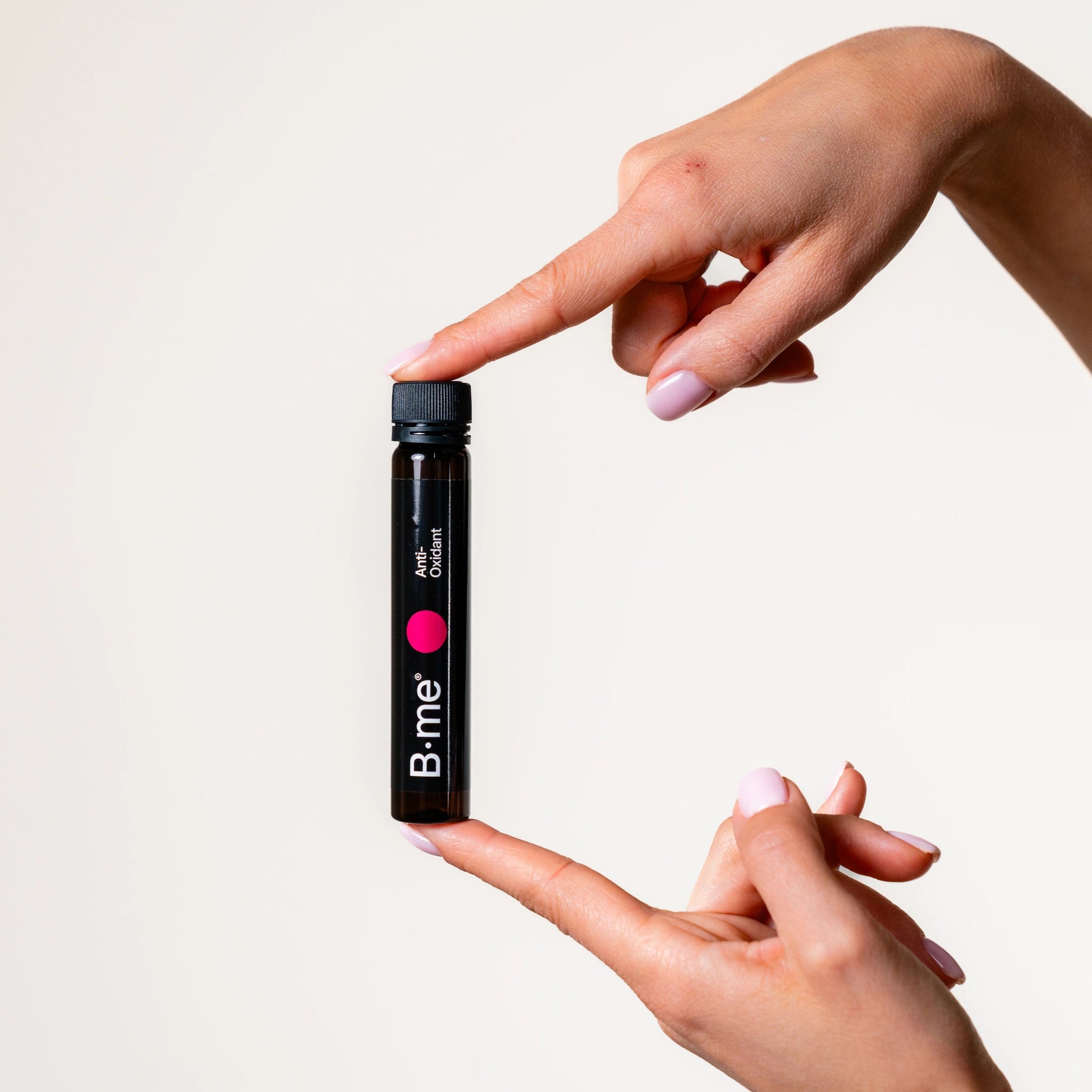 Two hands with pink gel nails holding B.me antioxidant supplement shot