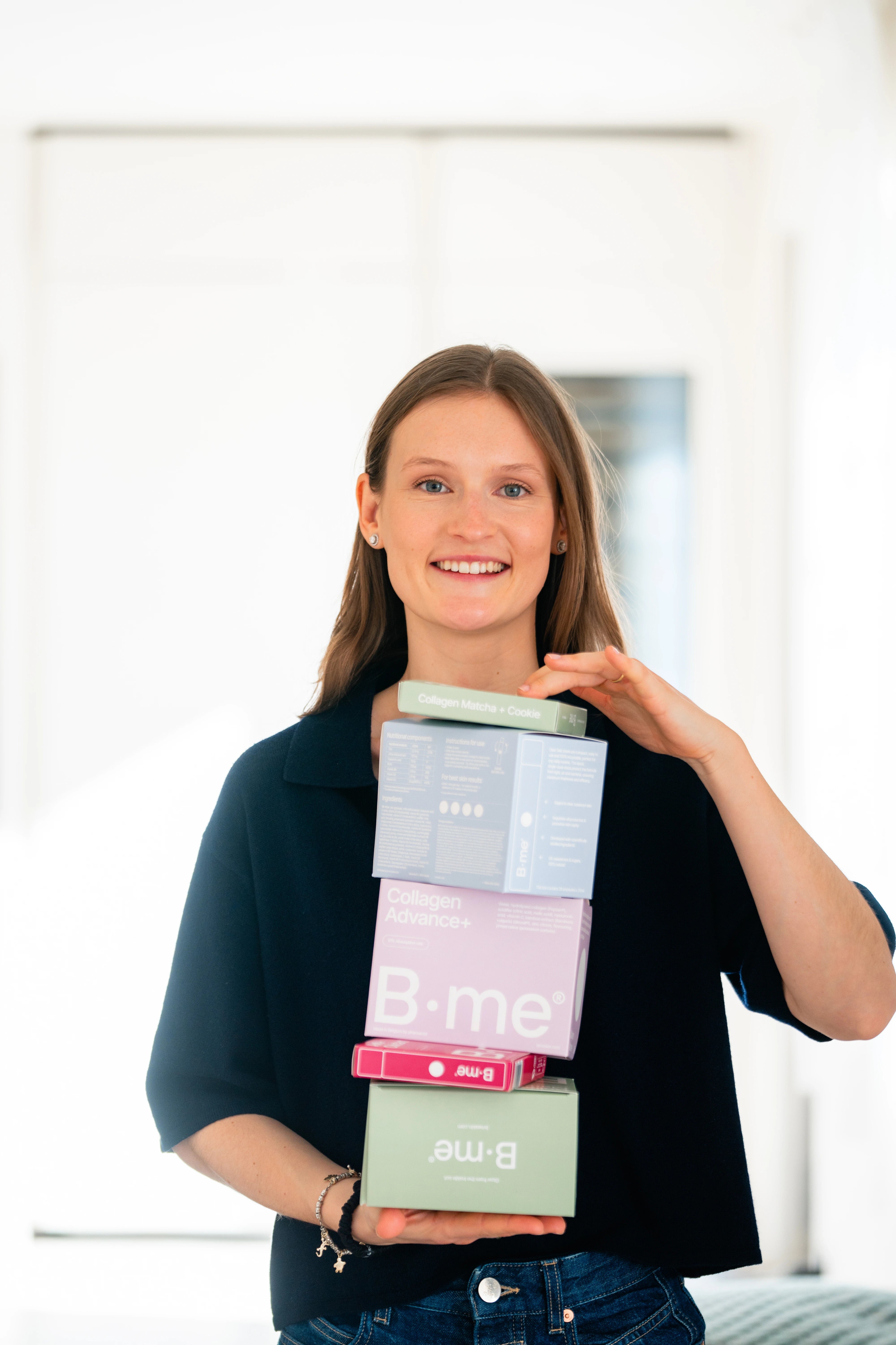 Camille, co-founder of B.me, smiling and holding product boxes in portrait format
