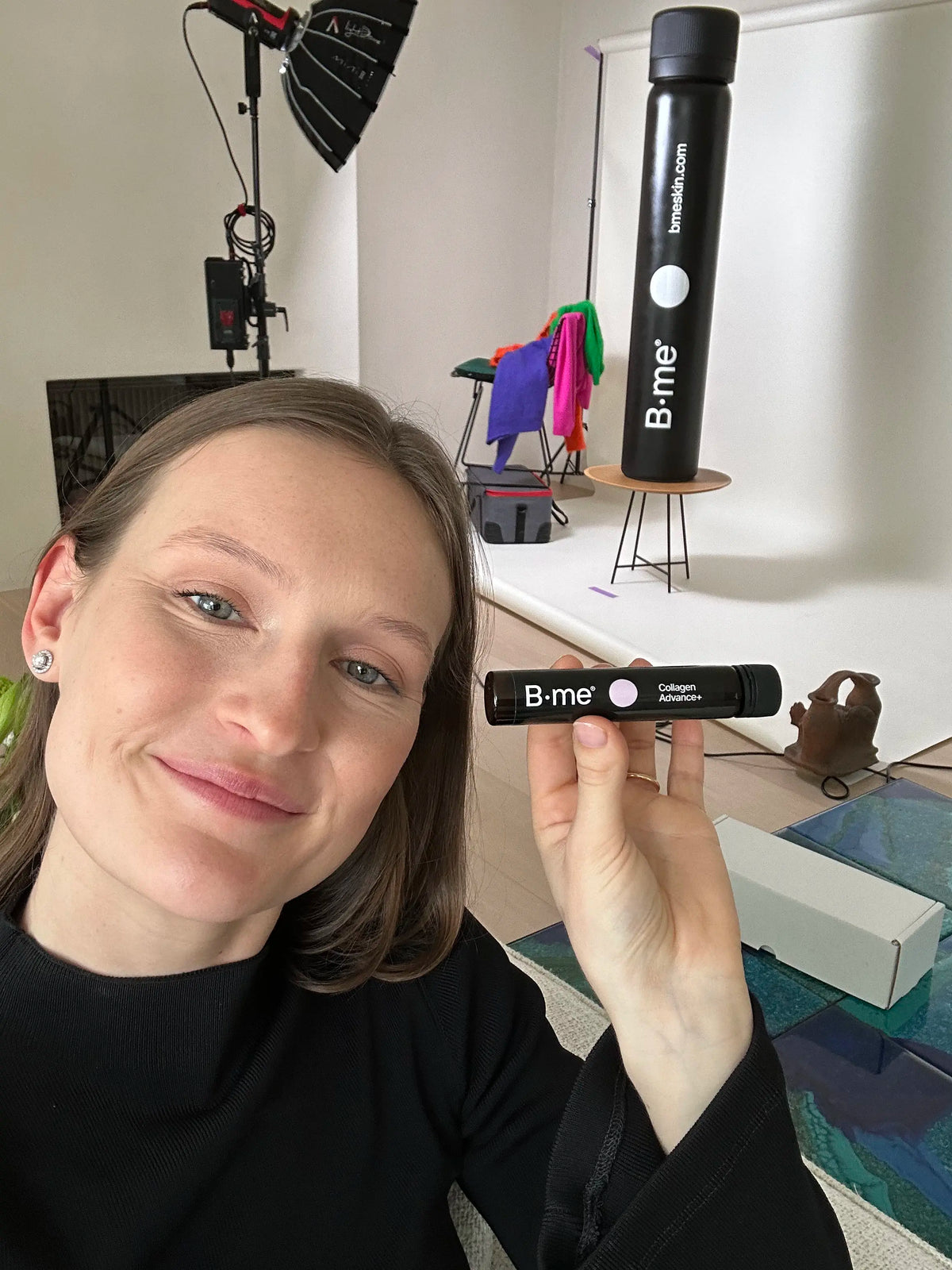 Camille, co-founder of B.me, taking a selfie while holding a supplement ampoule in a studio setting